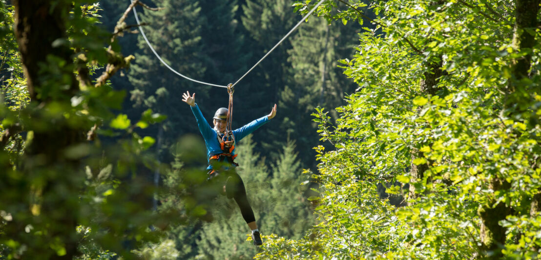 Eine Frau in sportlicher Kleidung hängt über einem Waldgebiet in der Zipline