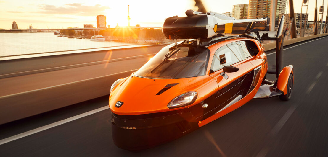 Ein orange-schwarzes Flugauto mit eingeklappten Propellern auf der Straße