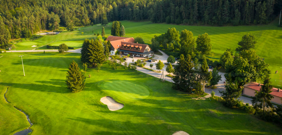 Blick auf Anwesen umgeben von Golfplatz mit Wald im Hintergrund