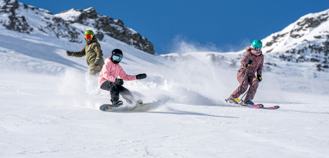 Ein Vater fährt mit seinen beiden Kindern die Piste hinunter