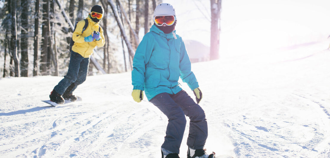 Zwei Menschen in Winterkleidung fahren auf Snowboards im Schnee