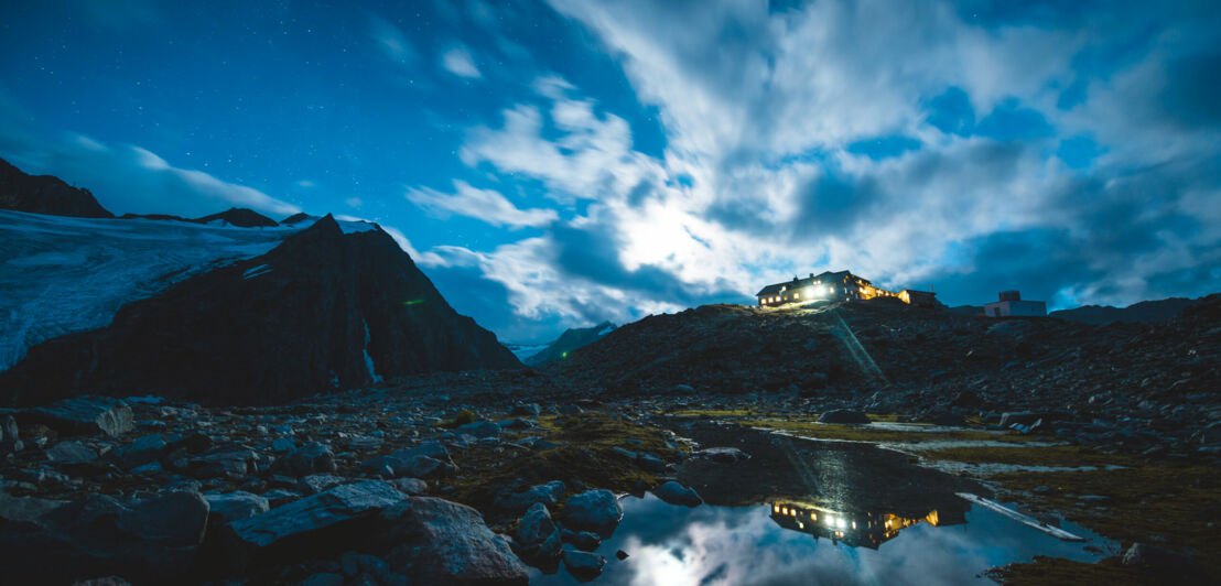 Eine erleuchtete Hütte in den Bergen bei Nacht.