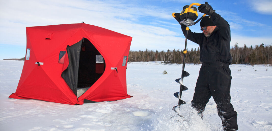 Ein Eisangler bohrt ein Loch in einen zugefrorenen See