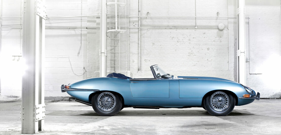 Ein blauer E-Type Roadster von der Seite in einem Industriebau