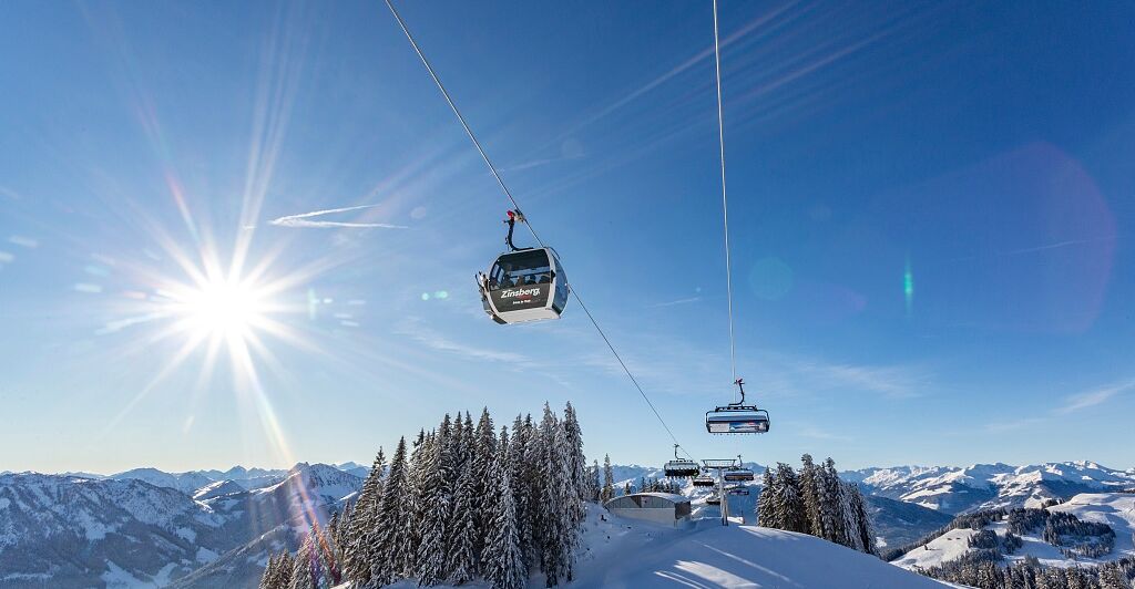 Zwei Menschen von hinten in einem Liegestuhl, sie blicken auf die verschneiten Berge des Skigebiets Wilder Kaiser