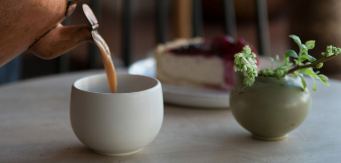 In einen Becher wird Tee aus der Kupferkanne gegossen