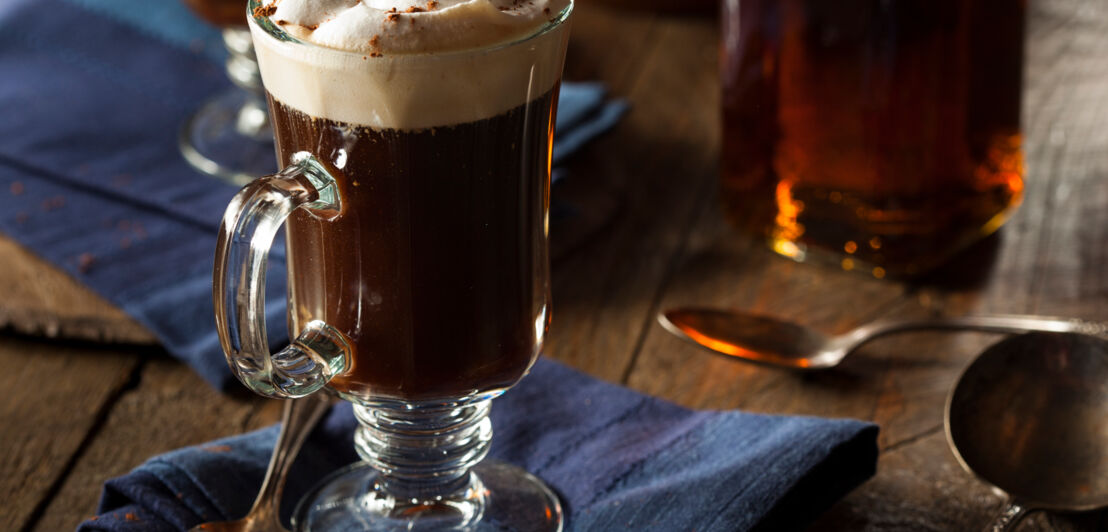 Ein Kaffeegetränk mit Sahne im Glas angerichtet auf blauer Stoffserviette