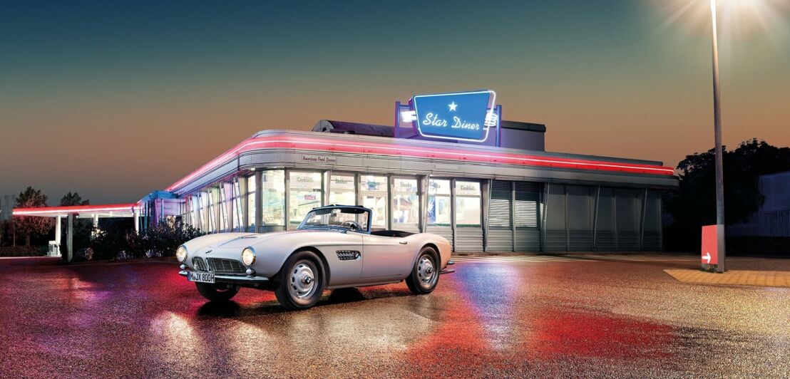 Der weiße BMW 507 steht vor einem amerikanischen Diner im Scheinwerferlicht