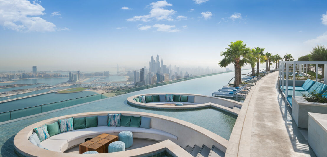 Ein langgestreckter Pool mit eingelassenen runden Sitznischen und Blick auf den Ozean sowie die Skyline Dubais