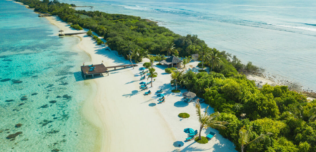 Aufsicht einer Landzunge mit weißem Sandstrand und grüner Vegetation im türkisblauen Meer, vereinzelt blaue Liegen am Strand