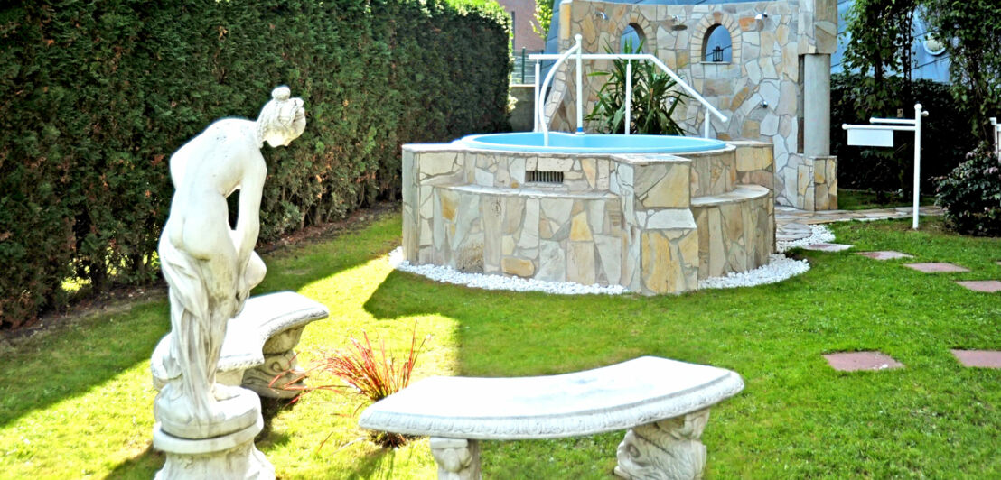 Whirlpool mit Mosaikfliesen in einem Garten mit einer Frauenstatue auf Sockel und zwei Bänken im antiken Design