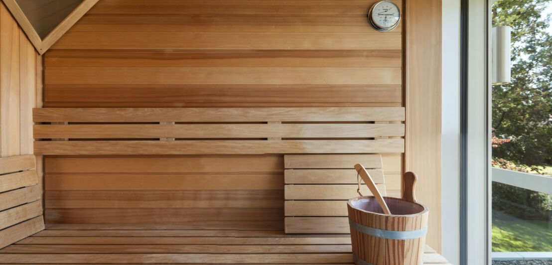 Holzsauna mit Holzeimer und Schhöpfkelle und einem Fenster zum Garten