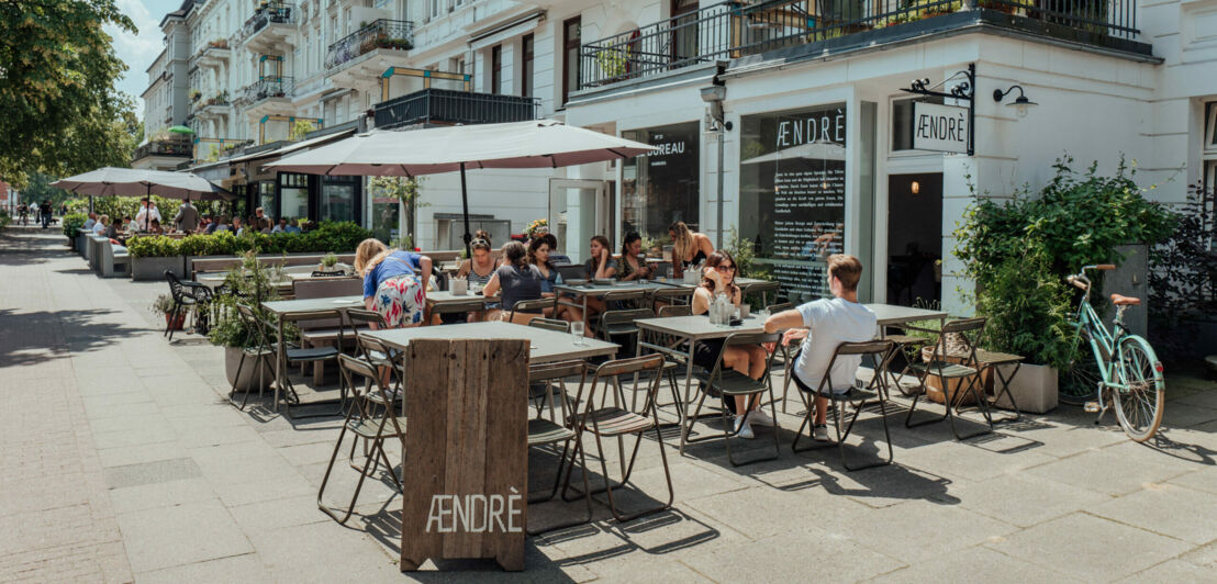 Außenaufnahme des Cafés Aendre mit Gästen auf der bestuhlten Terrasse bei Sonnenschein