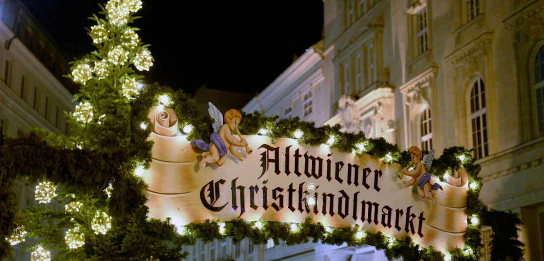 Das beleuchtete Eingangsschild des Altwiener Christkindlmarktes vor schmucken Häuserfassaden auf der Freyung