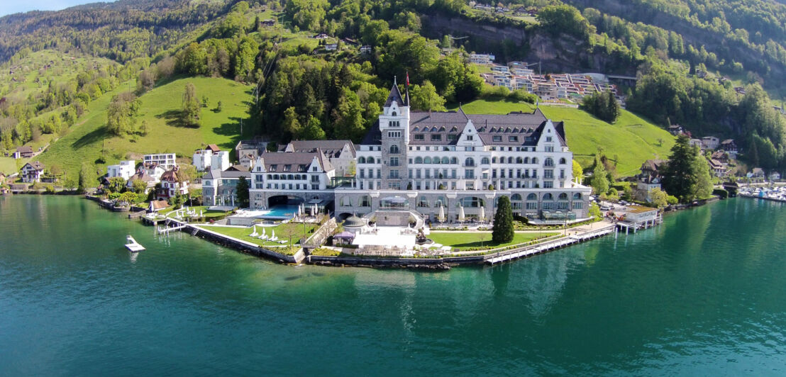 Panoramaaufnahme eines schlossartigen, luxuriösen Hotelkomplexes am Rande eines Seeufers und Berg im Hintergrund