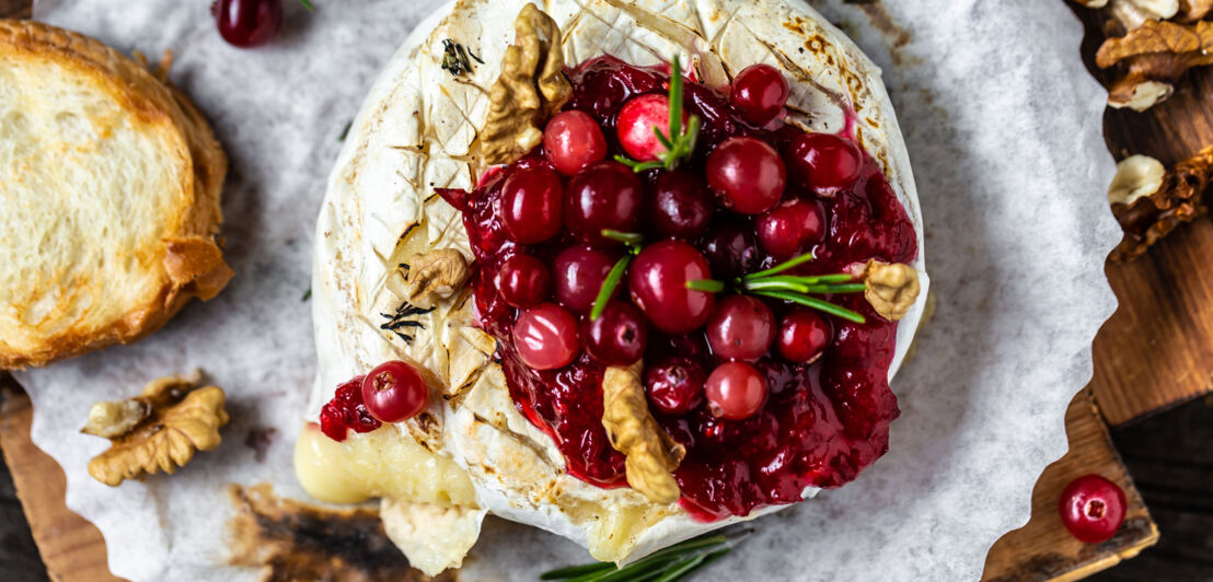 Traditioneller französischer gebackener Camembert mit Preiselbeeren und Nüssen angerichtet, garniert mit Rosmarin und Baguettebrot