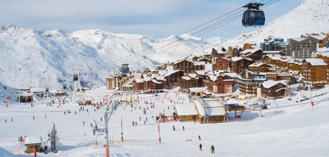 Eine Skipiste inklusive Gondelbahn vor einem Bergdorf und einer Gipfelkette