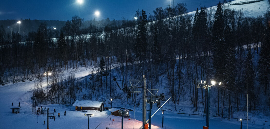 Mit Flutlicht beleuchtete Skipiste mit Sessellift bei Dunkelheit