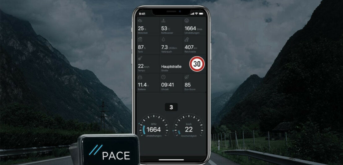 Ein OBD-2-Modul neben einem Smartphone, im Hintergrund eine Autobahn, die durch Berge führt