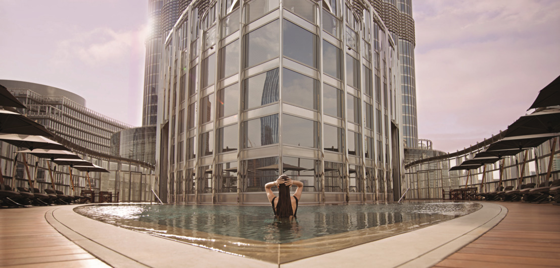 Eine Frau von hinten, die im Hotelpool steht, vor ihr ein verglastes Gebäude