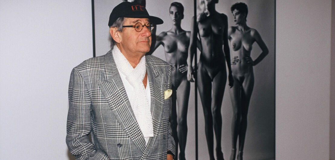 Helmut Newton vor einem seiner Fotos mit nackten Frauen