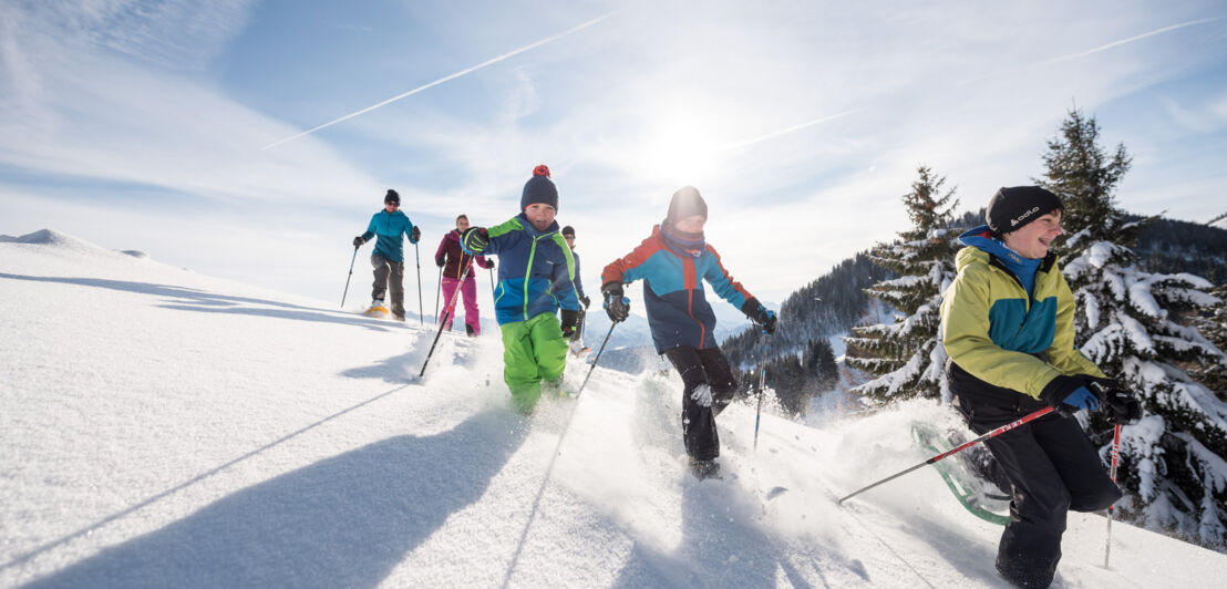 Kinder laufen mit Schneeschuhen bergab durch den Tiefschnee