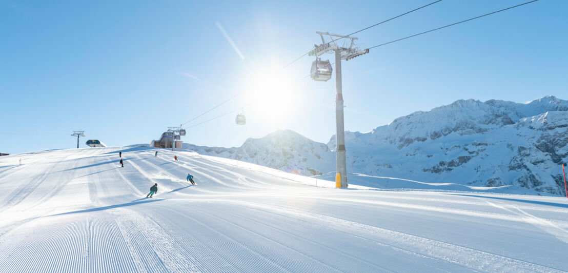 Eine präparierte Skipiste im Sonnenschein, darüber eine Gondelbahn