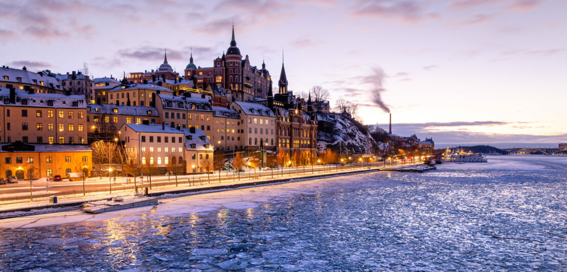 Ein Teil der pittoresken und eingeschneiten Insel Södermalm bei Dämmerung mit Eisschollen auf dem umliegenden Wasser