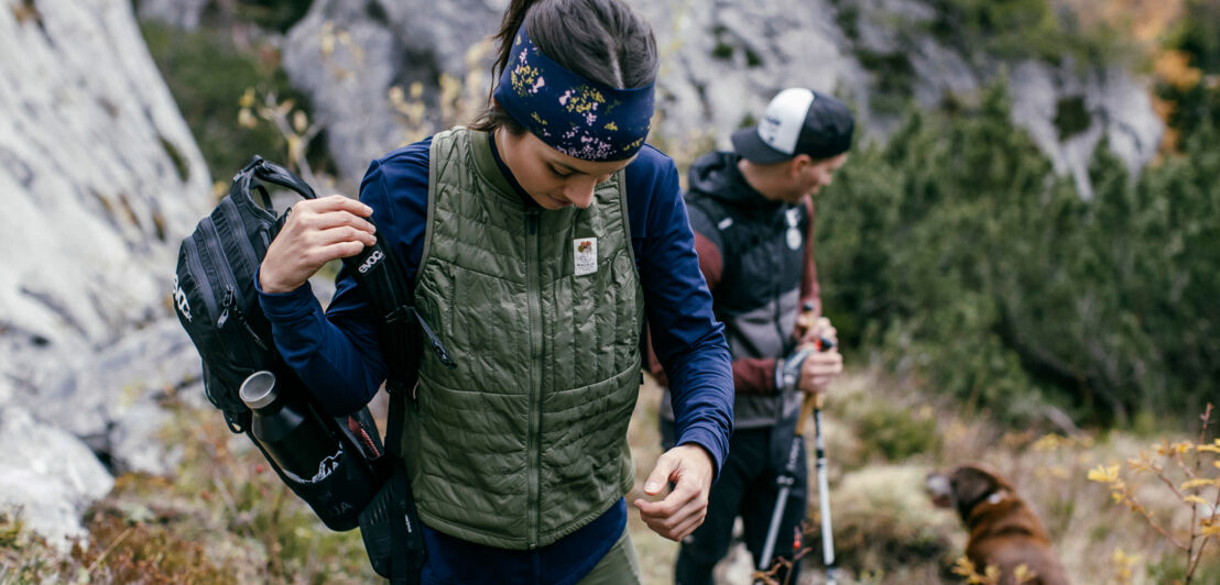 Eine Frau und ein Mann in Sportkleidung sind mit ihrem Hund in den waldreichen und herbstlichen Bergen unterwegs