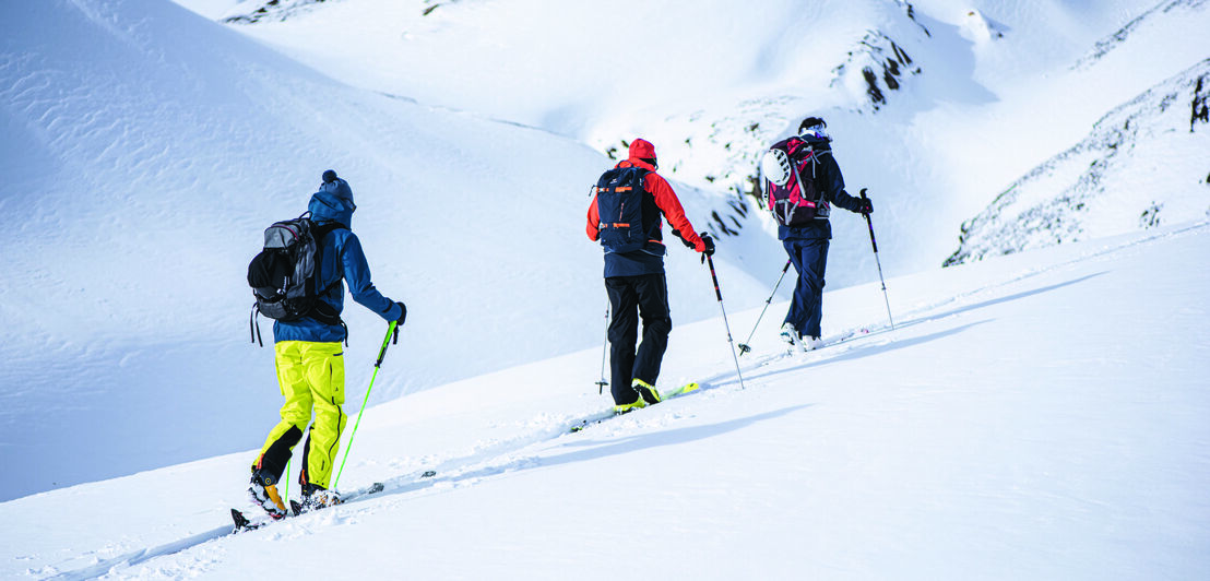 Drei Schneeschuhwander:innen auf einem verschneiten Berg