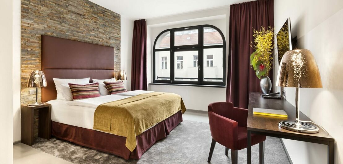 Innenansicht eines Hotelzimmers mit Doppelbett, kleinem Sessel und einem Tisch