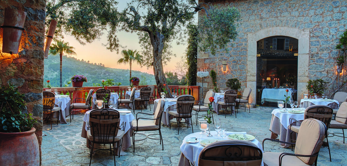 Eine mediterrane Terrasse mit Tischen, Stühlen und Bäumen in der Abendsonne