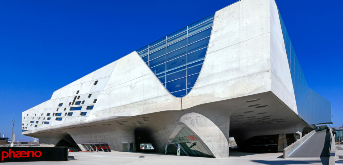 Ein großes, modernes und freistehendes Gebäude aus Beton und Glas mit Vorplatz