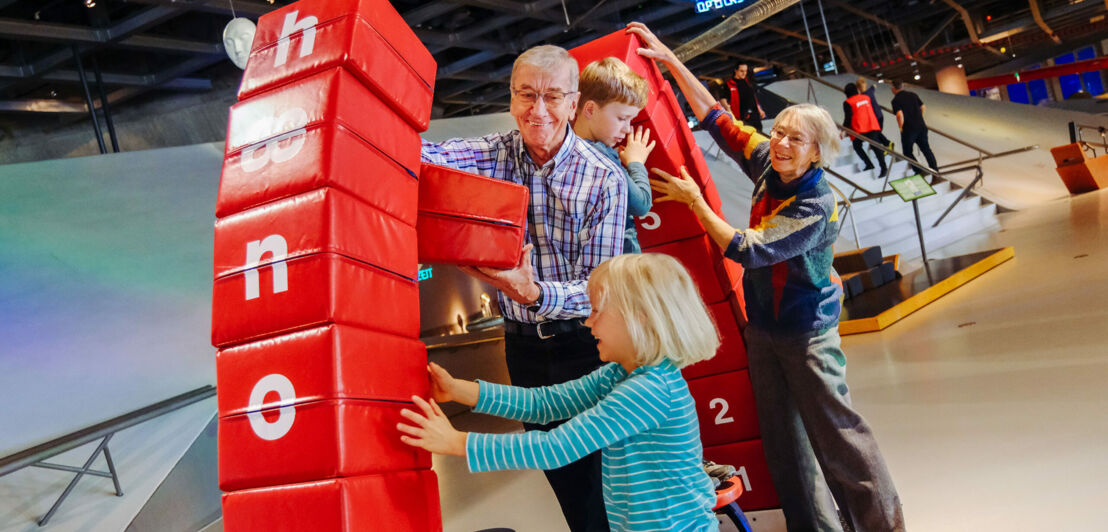 Zwei Kinder und ihre Großeltern bauen einen Brückenbogen aus Schaumstoffelementen in einem Bildungszentrum