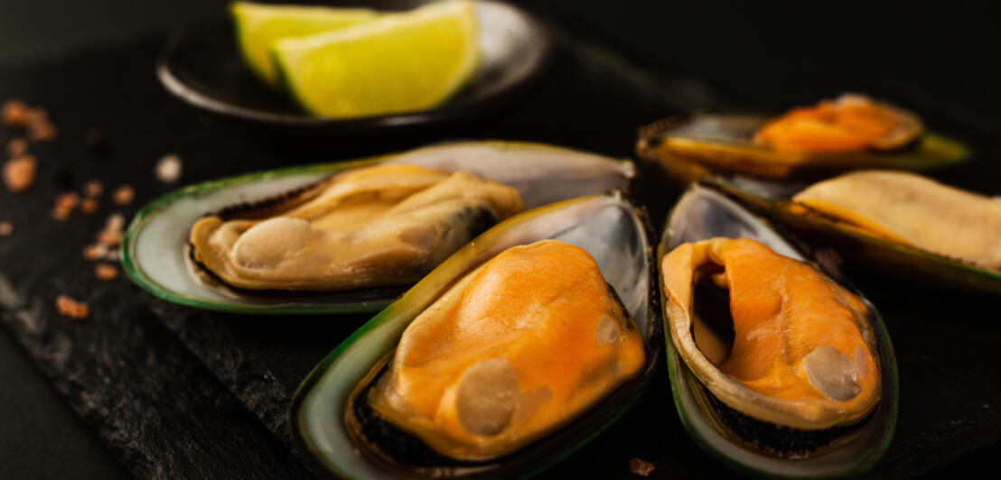 Grünschalmuscheln mit Zitrone auf einer schwarzen Platte