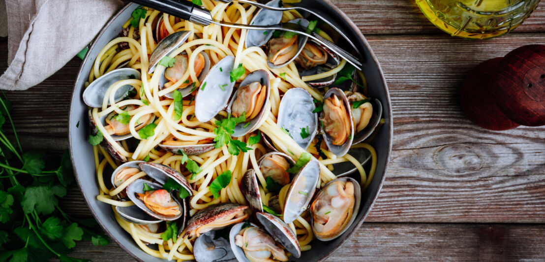 Spaghetti alle vongole im Teller angerichtet auf einer Holztafel