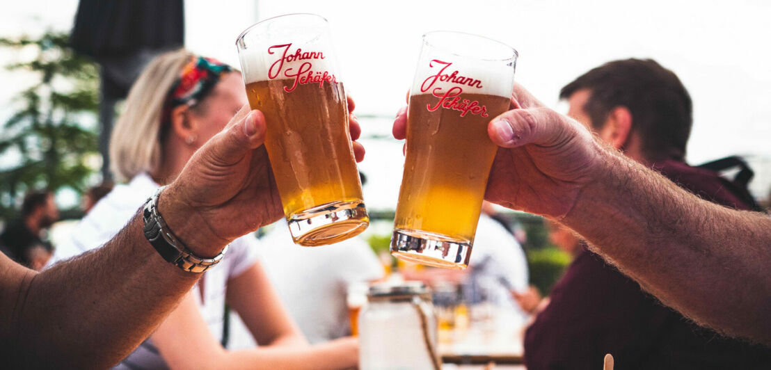 Zwei Menschen prosten sich mit einem gezapften Bier im Glas zu