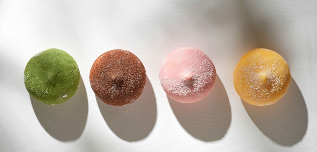 Auf einer hellen Unterlage liegen gefärbte und bestäubte Mochi-Eiskugeln.