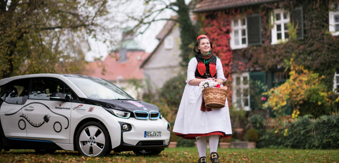 Eine als Rotkäppchen verkleidete Frau neben einem E-Auto