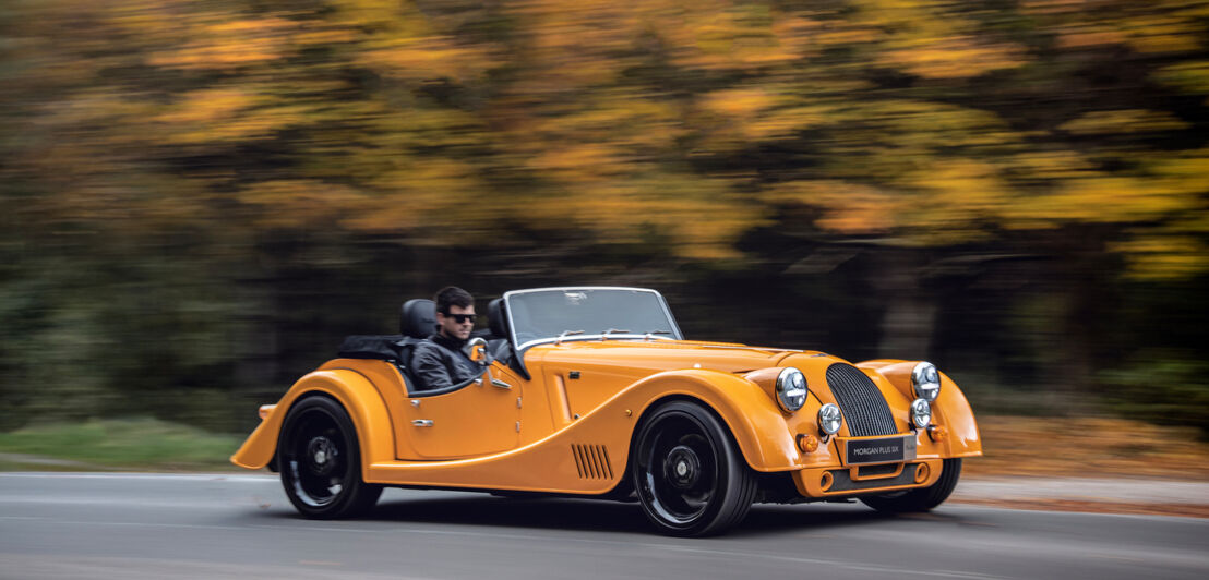 Ein gelber Roadster fährt auf einer Straße entlang.