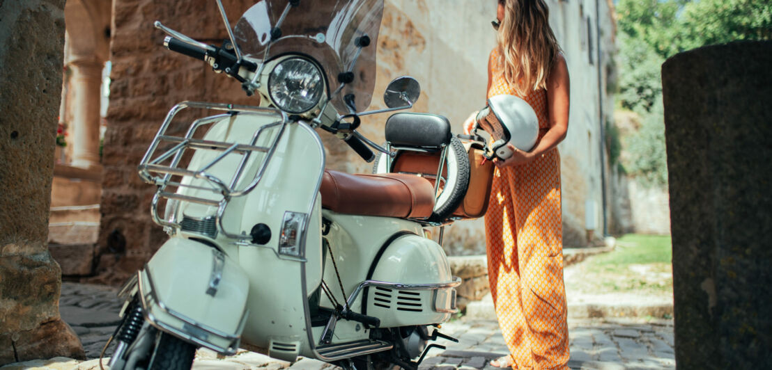 Depicting a beautiful woman on a vespa, cruising through old city town.