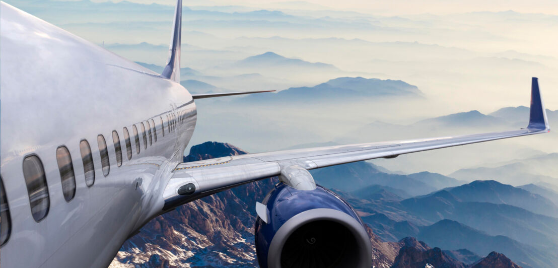 Luftaufnahme eines fliegenden Flugzeuges über einer wolkenverhangenen Gebirgslandschaft