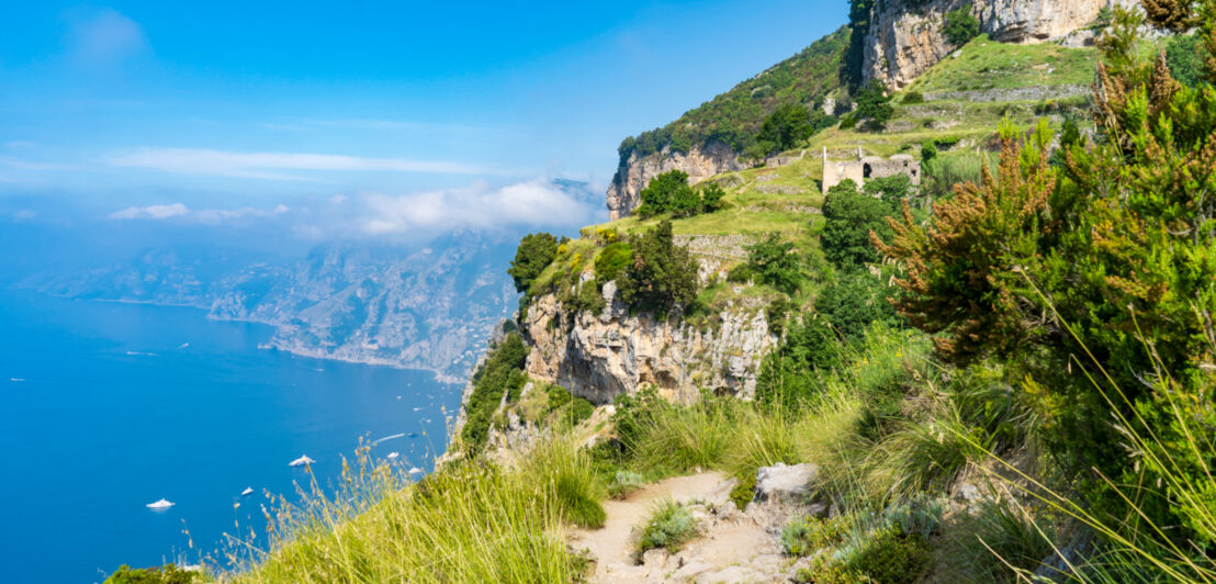 Unbefestigter Wanderweg in den Bergen mit Blick aufs Meer.