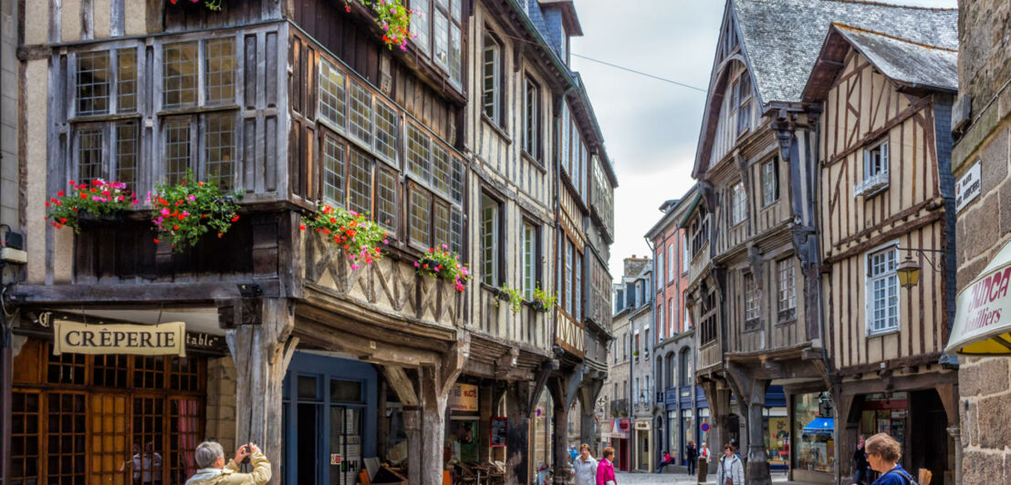 Eine Fachwerkgasse in Dinan, im Vordergrund wirbt ein Schild für eine Crêperie.