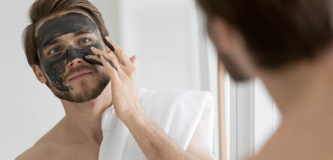 Ein junger Mann trägt eine schwarze Gesichtsmaske auf und hat dabei ein Handtuch über seiner Schulter.