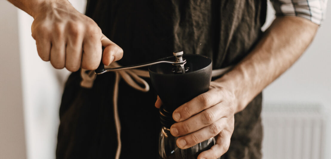 Ein Mann bedient eine manuelle Kaffeemühle.