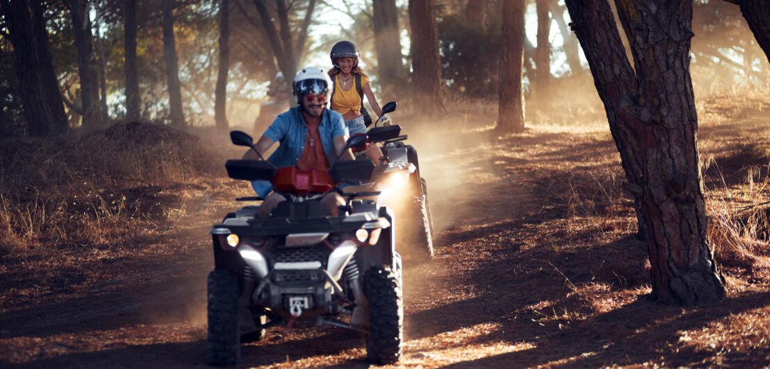 Zwei Menschen fahren mit dem Quad durch einen Wald