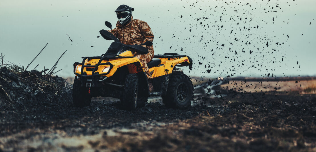 Ein Mensch in Schutzkleidung wirbelt mit dem Quad Matsch auf