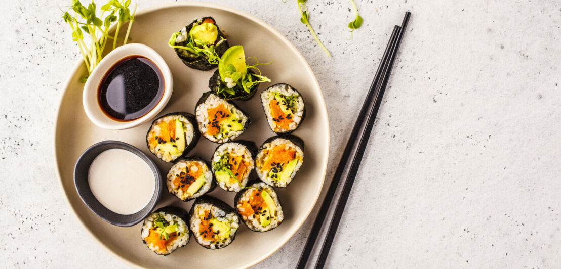 Vegane Sushi-Rollen auf einem Teller mit Sojasauce, Dip und Stäbchen