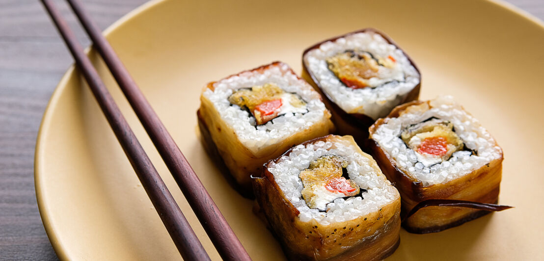 Veganes Sushi auf einem runden Teller mit Stäbchen